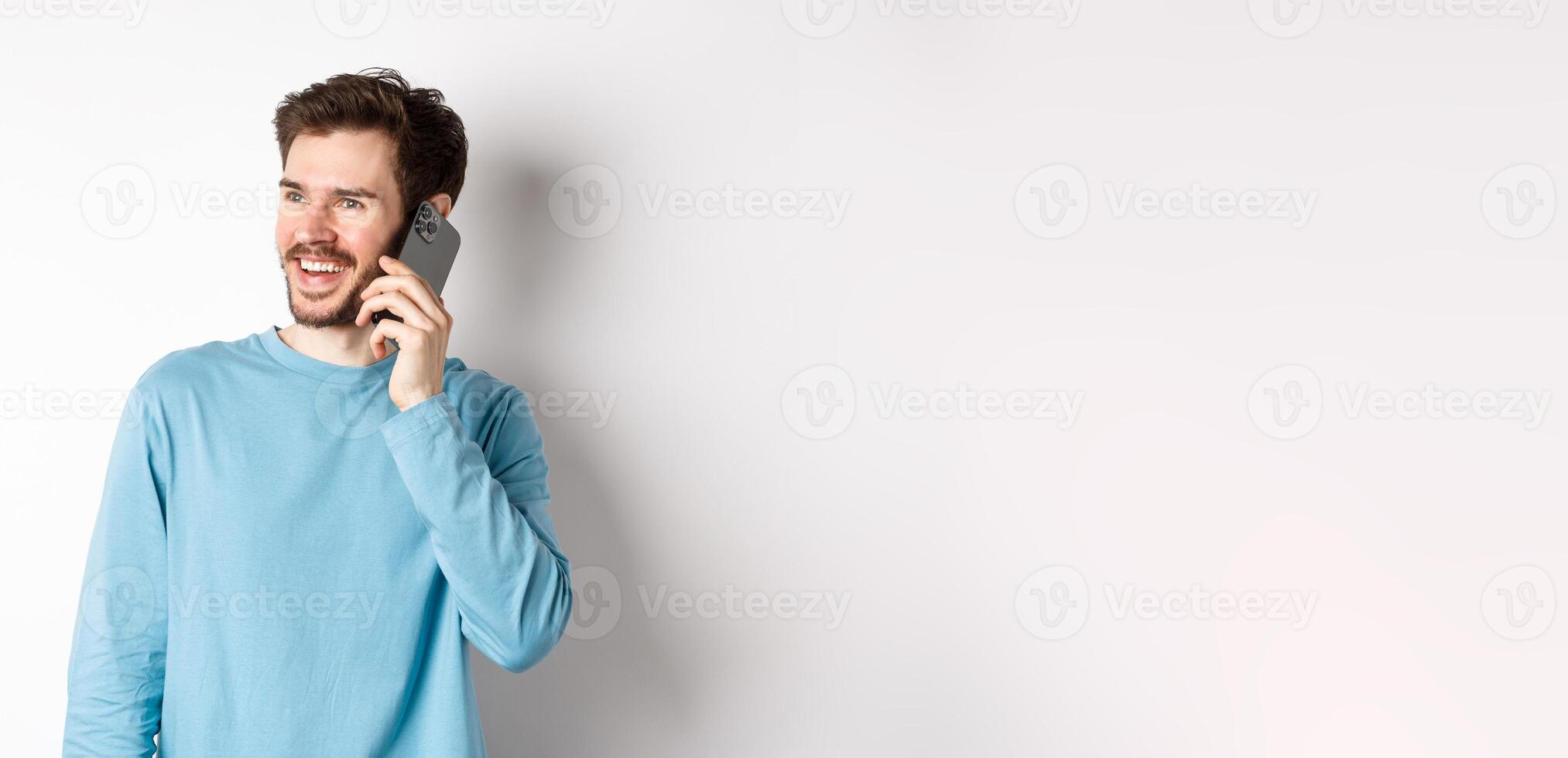 Technology concept. Joyful man enjoying phone call, talking on smartphone and smiling, standing in casual shirt over white background photo