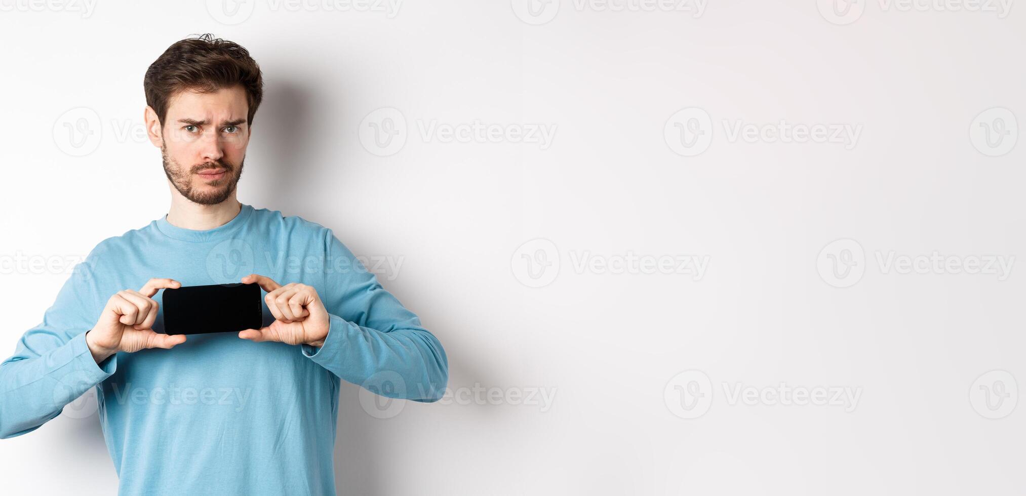 E-commerce and shopping concept. Sad and disappointed guy complaining, showing empty smartphone screen, standing on white background photo