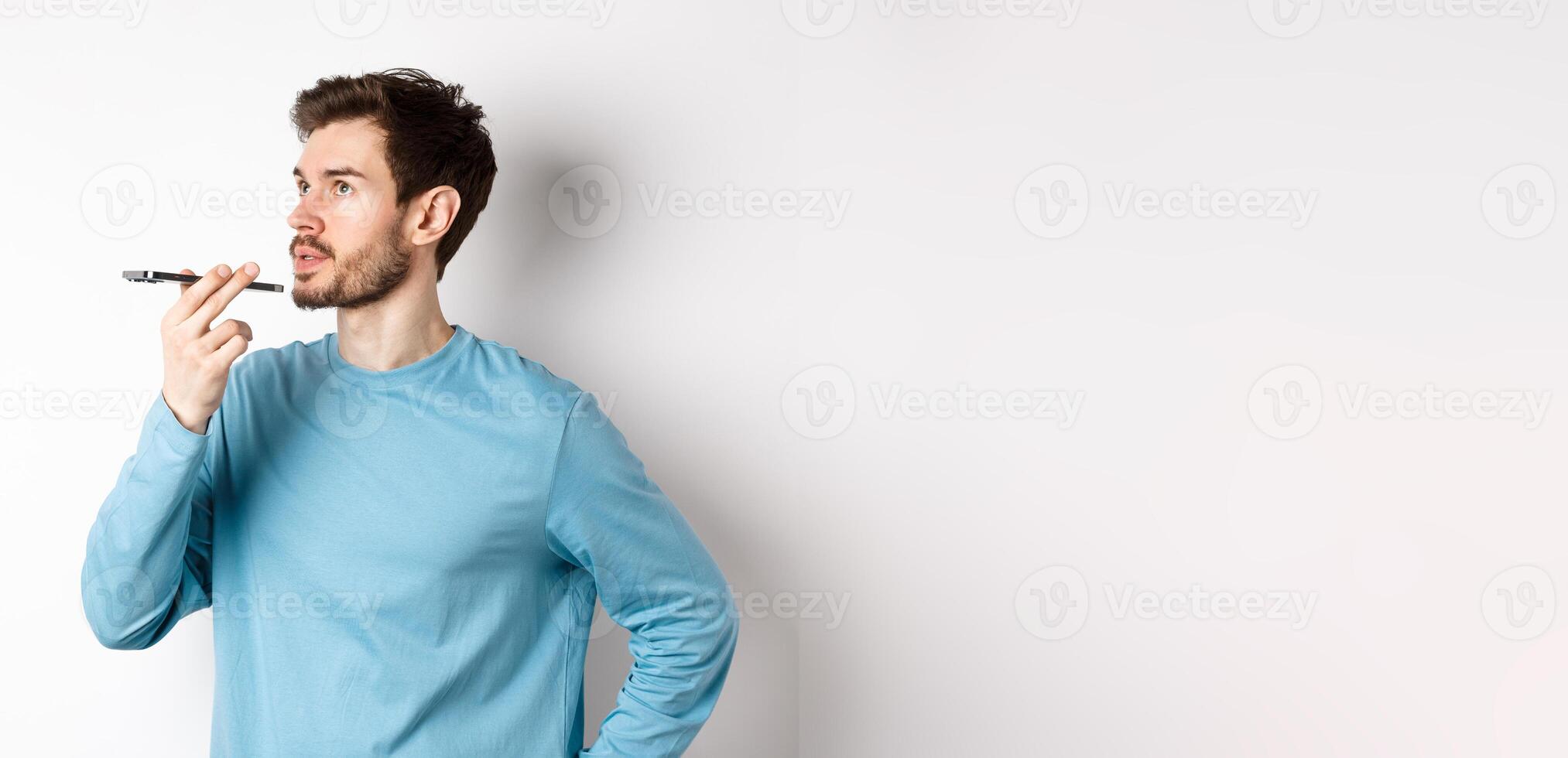 Handsome young man recording voice message on smartphone, holding phone near lips and talking. Guy using translator app on mobile phone, white background photo