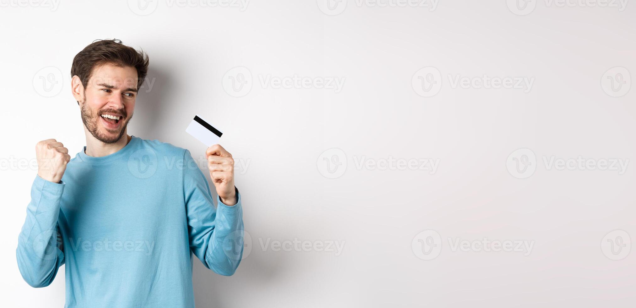 Happy man dancing with plastic credit card, smiling and saying yes, celebrating on white background photo