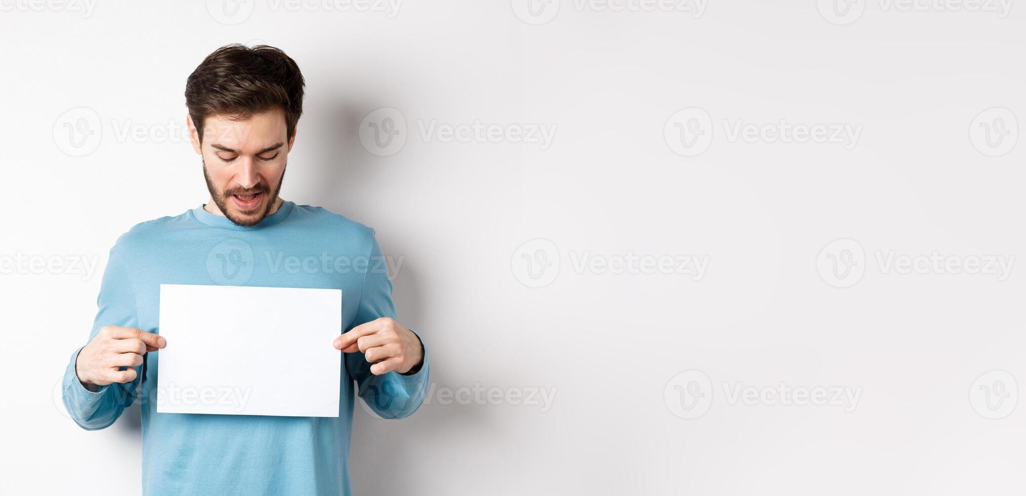 Excited bearded guy reading banner on blank piece of paper, showing logo, standing over white background photo