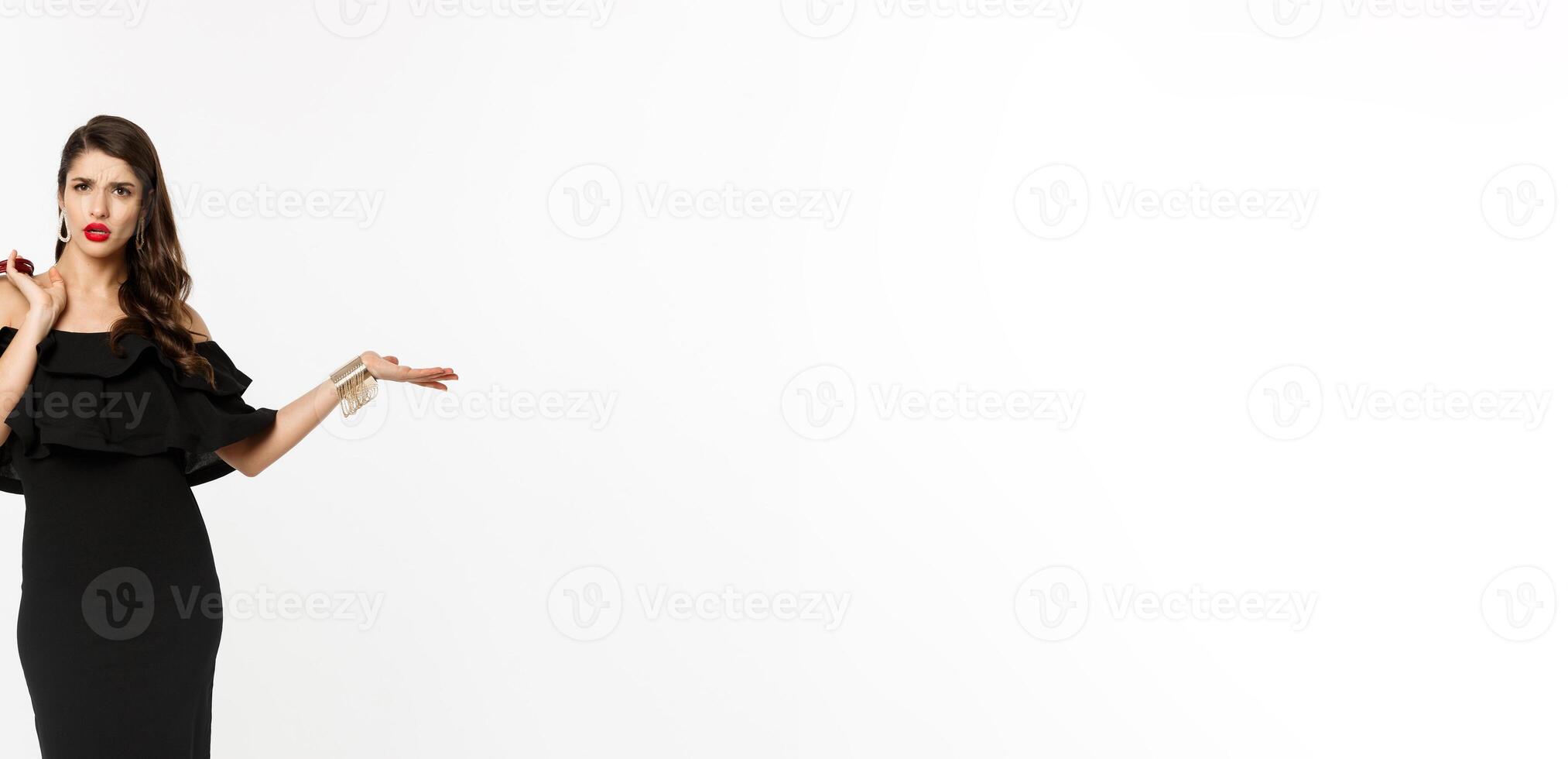 Beauty and fashion concept. Full length of arrogant and sassy woman in black dress, holding purse on shoulder and stroll forward at camera, posing over white background photo