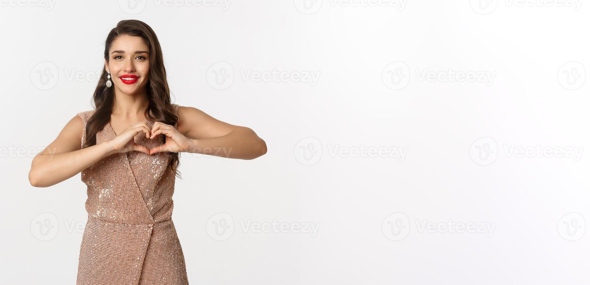 Celebration and party concept. Beautiful young woman in elegant dress showing heart sign, I love you gesture, express sympathy and smiling, white background photo