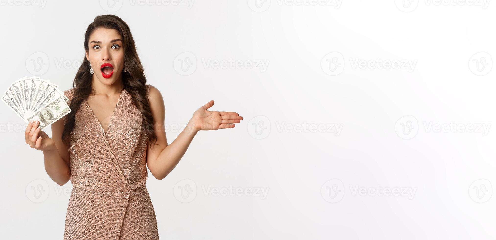 Shopping concept. Elegant woman in glamour dress holding money and looking surprised. winning prize, standing over white background photo