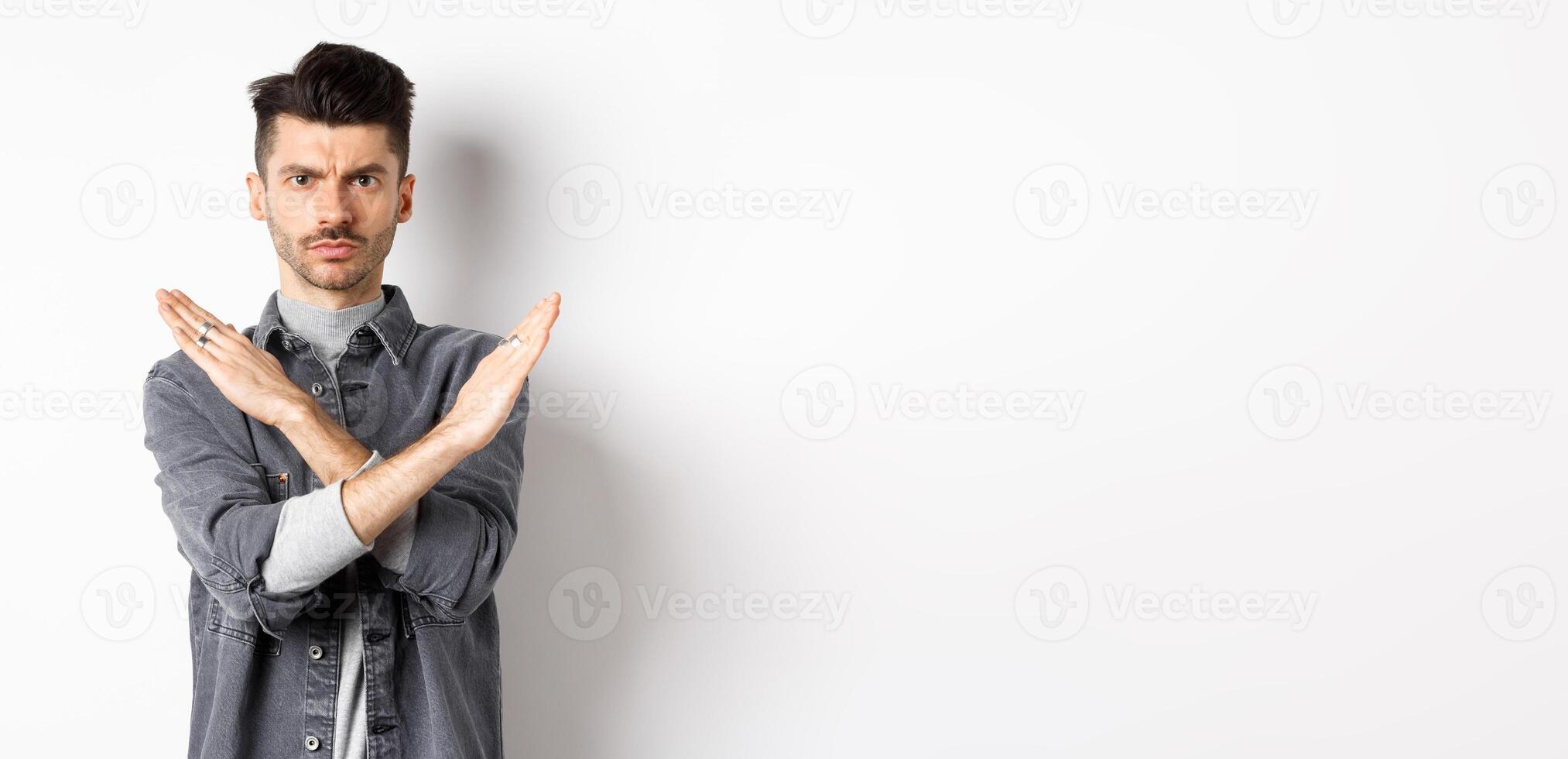 Angry man show cross gesture to stop or say no, frowning and looking serious, disagree and prohibit bad situation, standing on white background photo