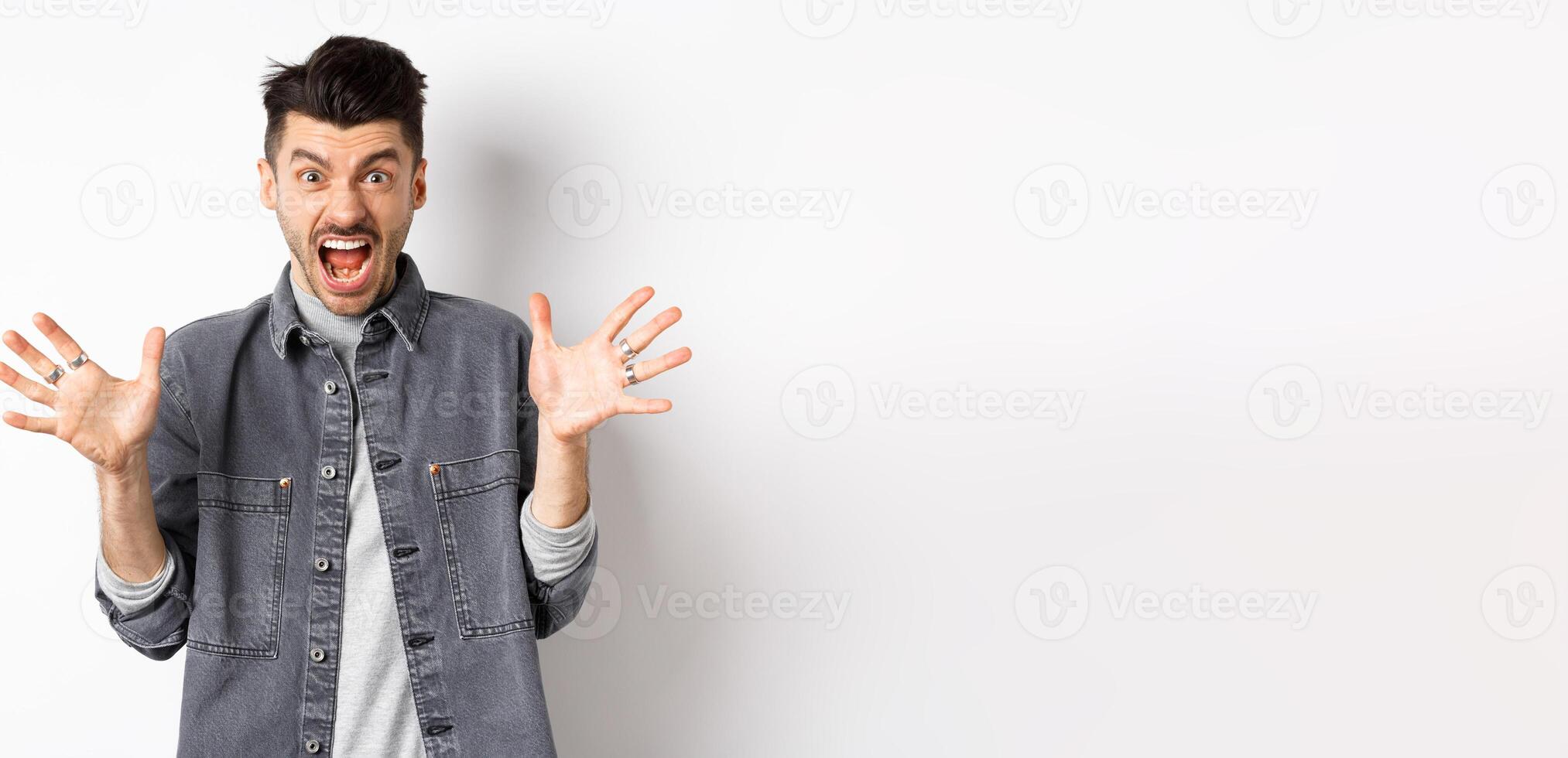 Angry man scream and look scary at camera, shouting with furious and hateful expression, standing on white background photo