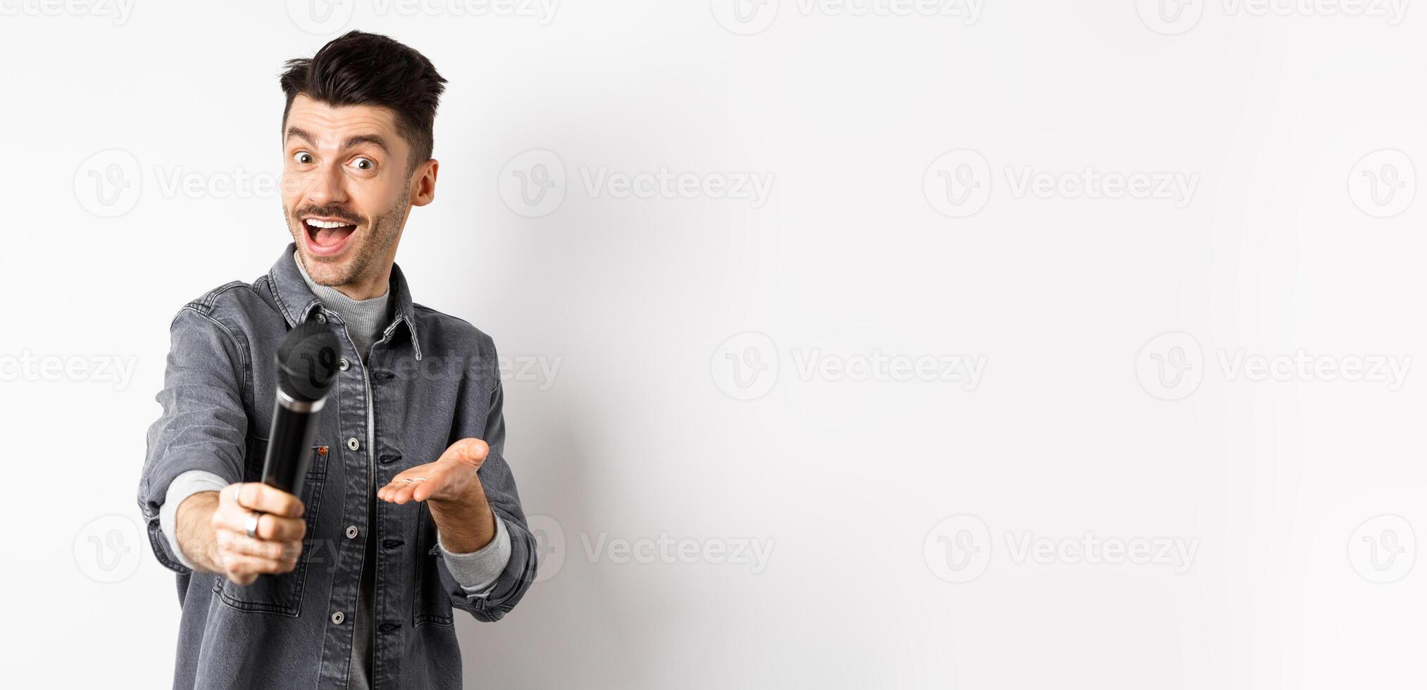 Handsome smiling man stretch out hand with microphone, giving you mic, standing on white background photo