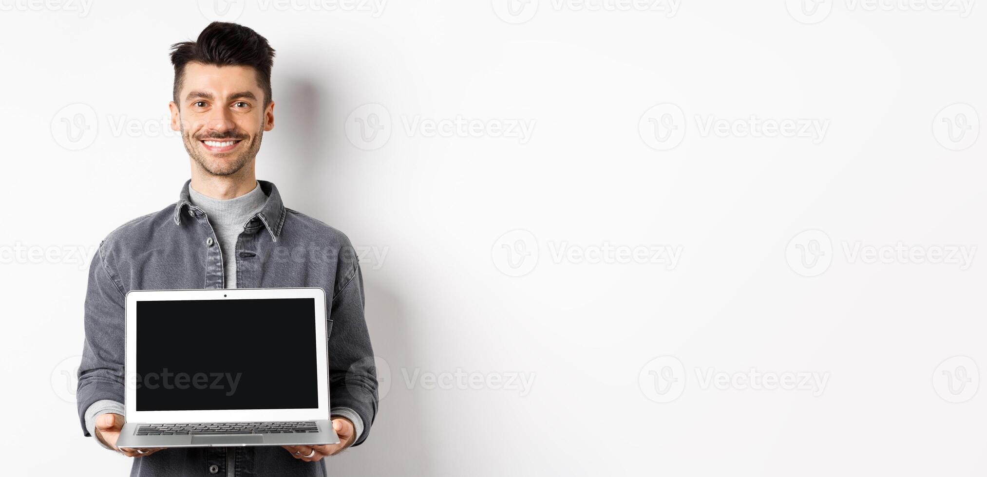 Smiling young man showing empty laptop screen, showing online deal, standing on white background photo