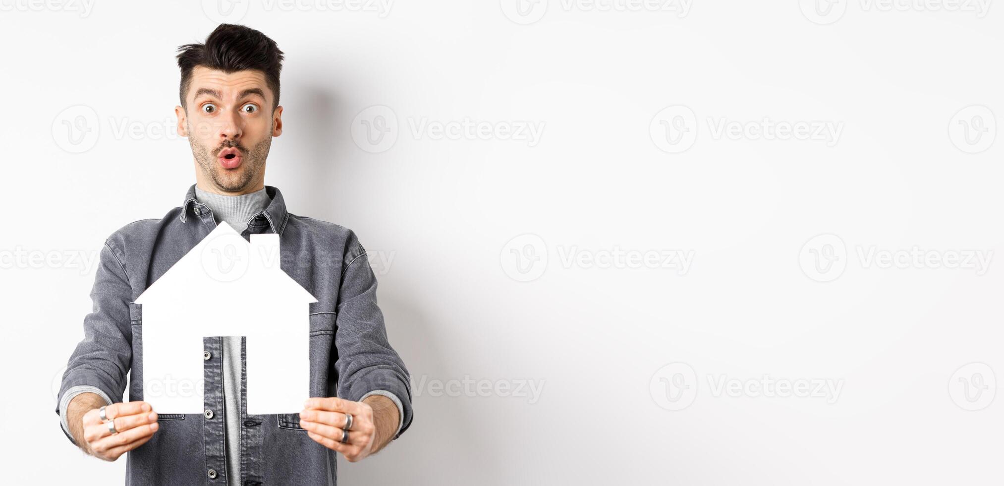 Real estate and insurance concept. Excited man showing paper house cutout and say wow, checking out apartment or property, standing amazed on white background photo