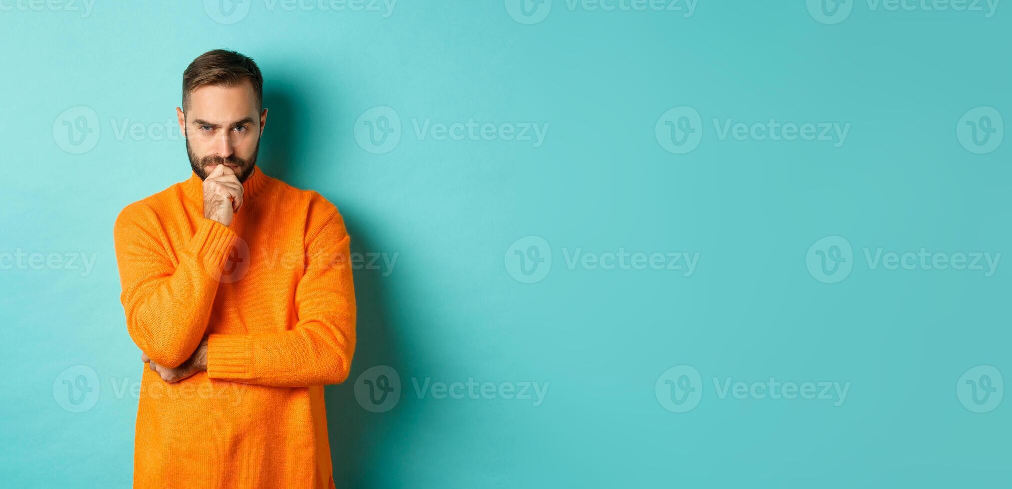 Thougtful young man making decision, looking serious and thinking, choosing, standing near copy space turquoise background photo
