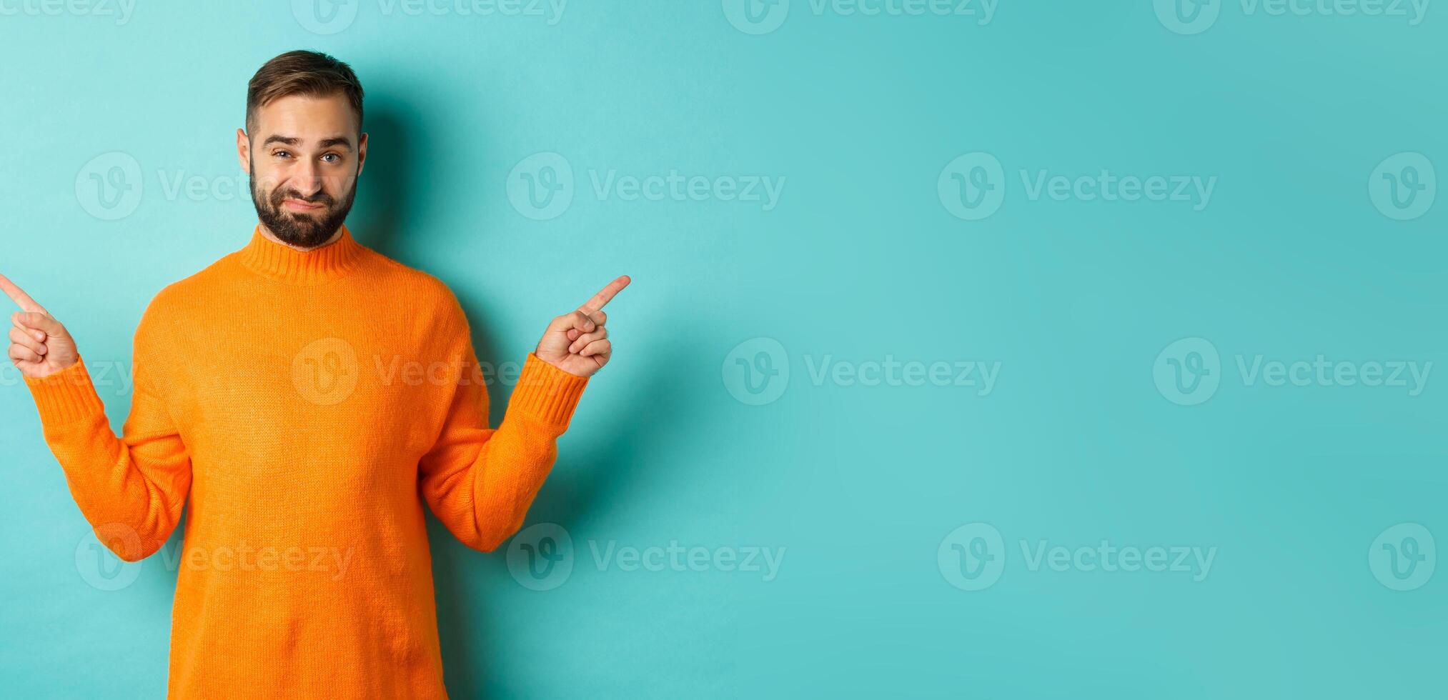 Doubtful and indecisive man pointing fingers sideways, showing different sides, two choices, looking skeptical, standing over light blue background photo