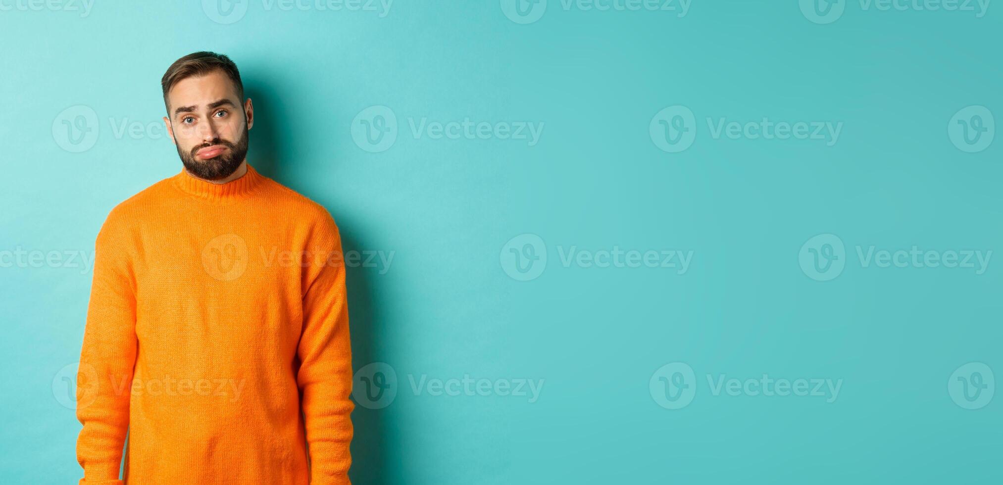 Sad man looking at camera, sulking and feeling distressed, standing over light blue background photo