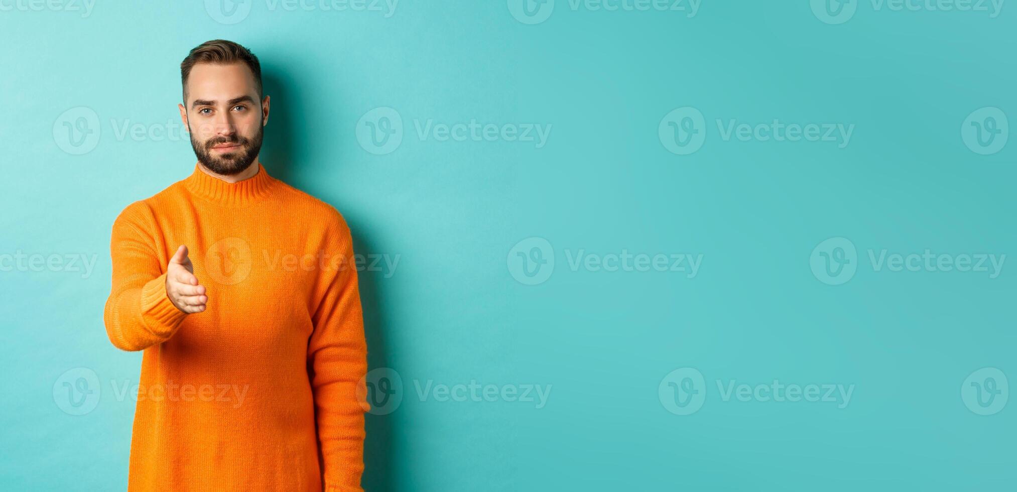 Confident man extending hand for handshake, greeting you, looking self-assured, standing over light blue background photo