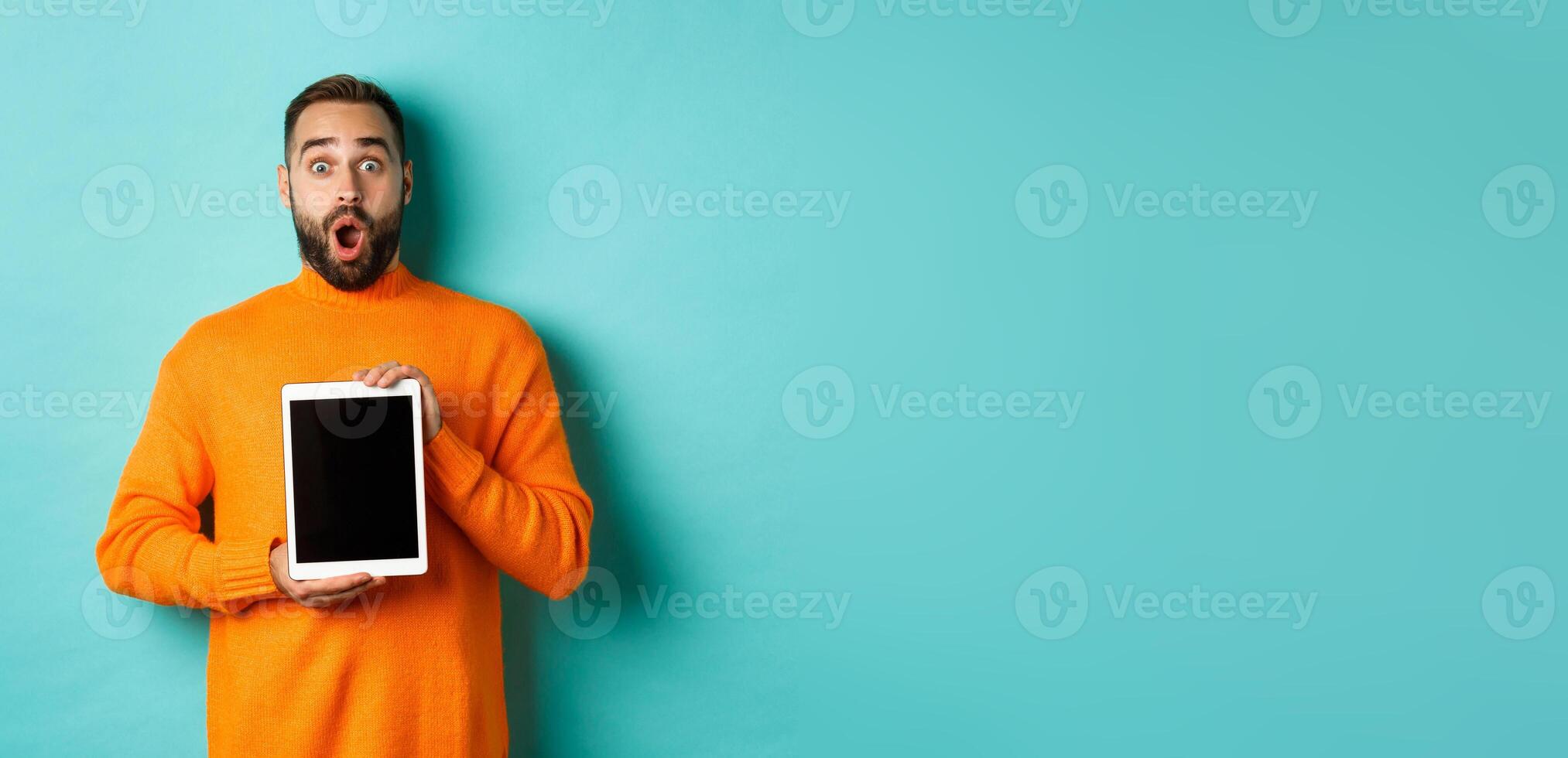 Technology. Surprised bearded man drop jaw, staring at camera and showing digital tablet screen, standing againt light blue background photo