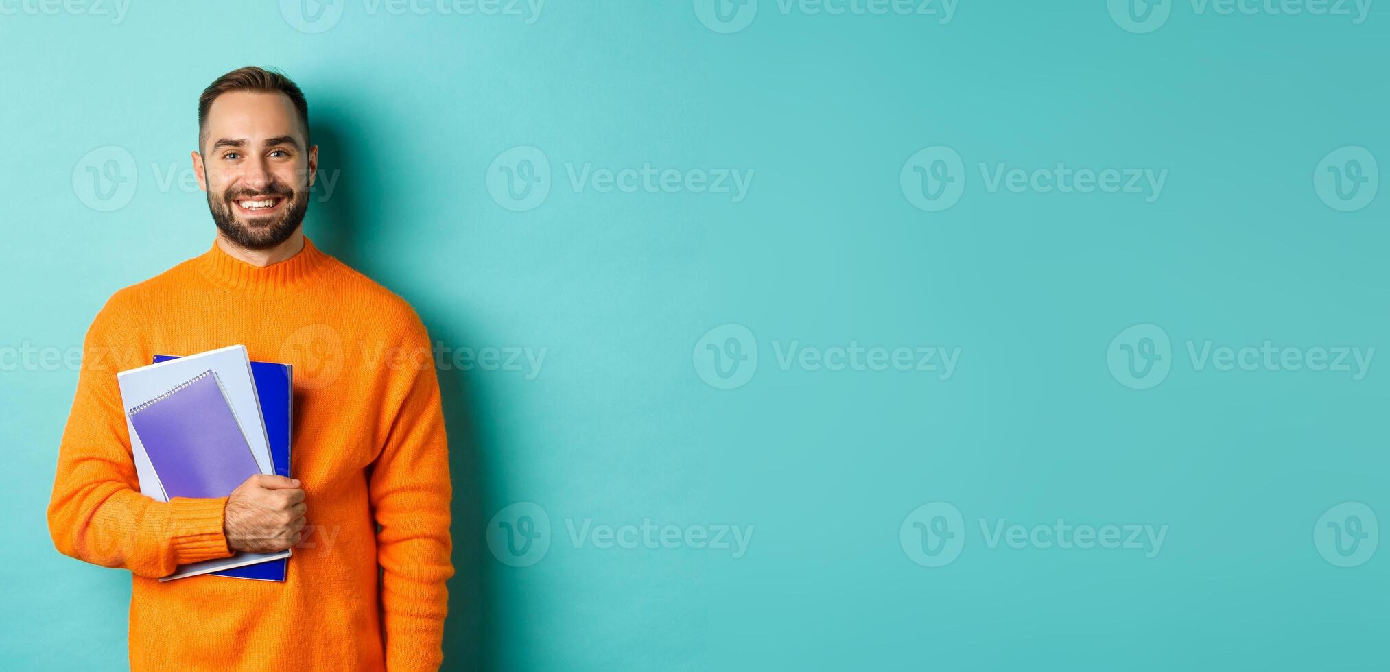 Education. Smiling bearded man holding notebooks and smiling, going on courses, standing over light blue background photo