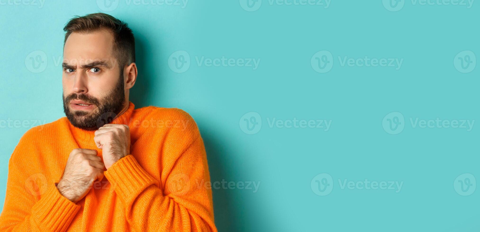Close-up of scared bearded man looking startled and displeased, jumping from fear, standing over light blue background photo