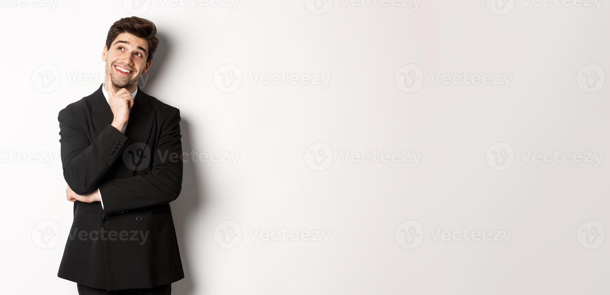 Portrait of thoughtful smiling man in stylish party suit, looking at upper left corner and thinking, imaging things, standing over white background photo