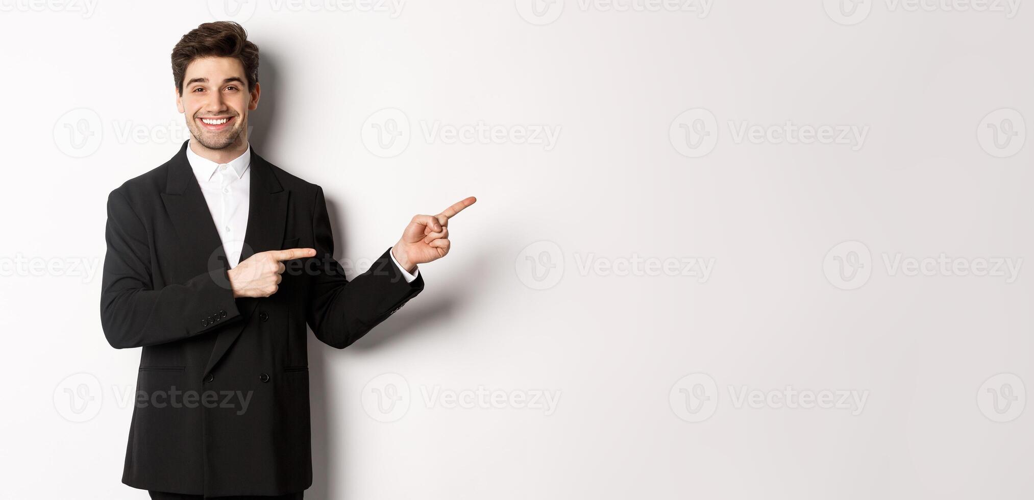 Image of attractive smiling guy dressed for new year party, pointing fingers right and showing advertisement, standing over white background photo