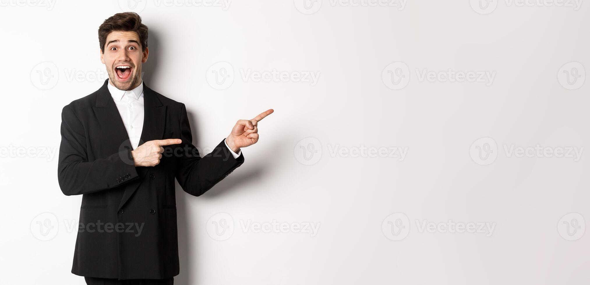 Image of attractive smiling guy dressed for new year party, pointing fingers right and showing advertisement, looking impressed standing over white background photo