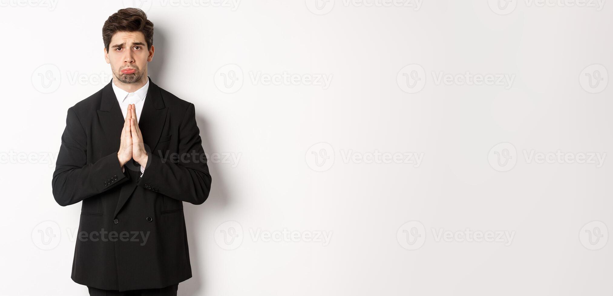 Miserable clingy guy need help, pouting silly and begging for something, asking for favour, standing against white background in black suit photo