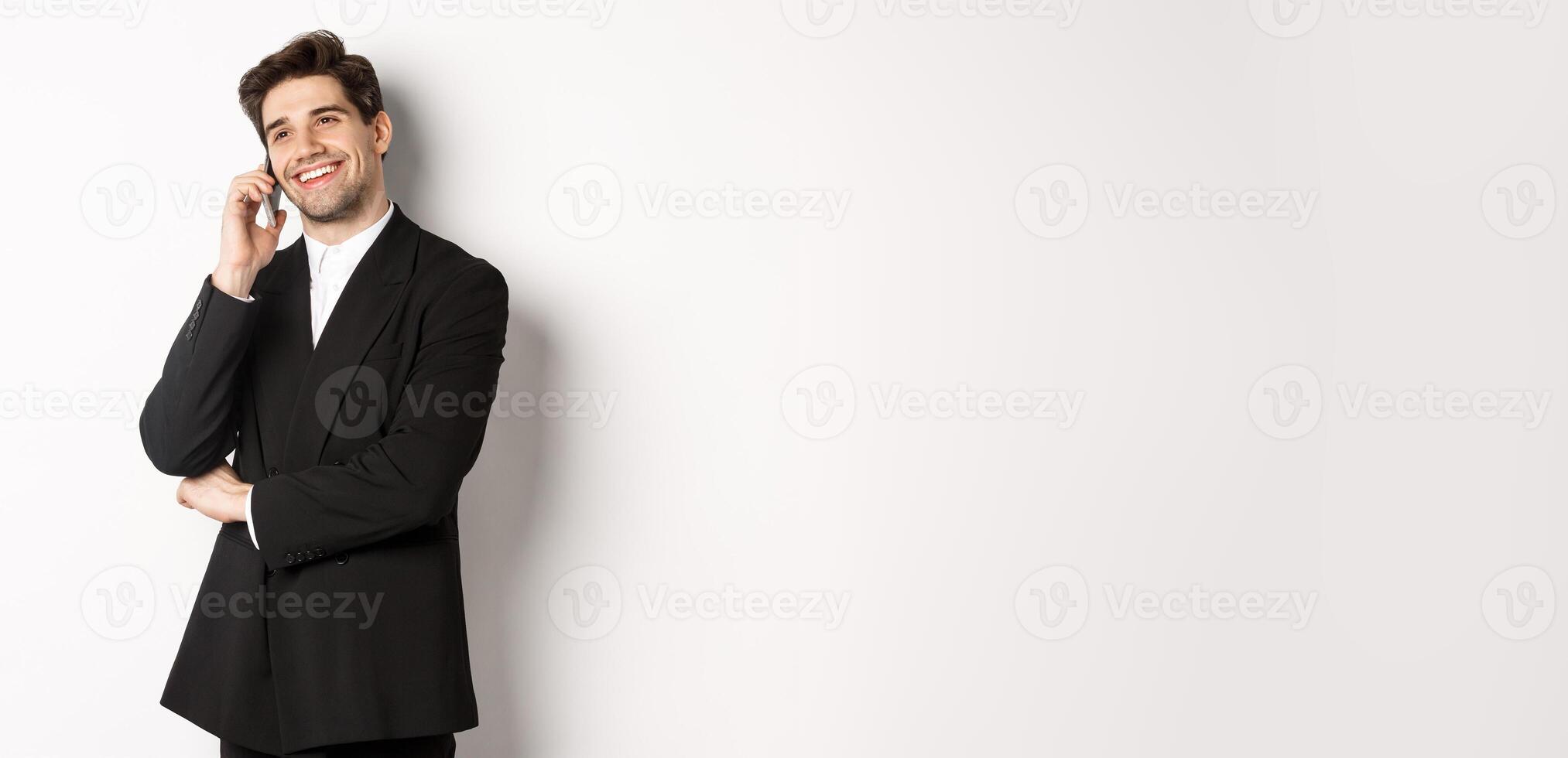 Image of handsome and successful businessman talking on phone, smiling pleased, standing in suit against white background photo
