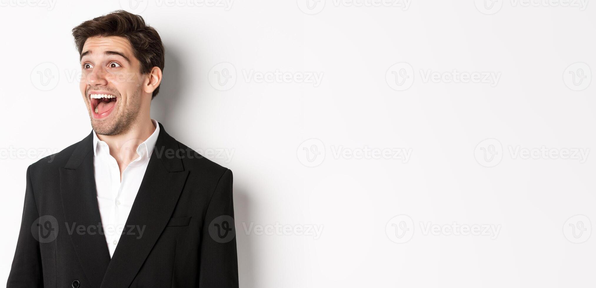 Close-up of handsome male entrepreneur in suit, looking left and smiling amazed, standing against white background photo