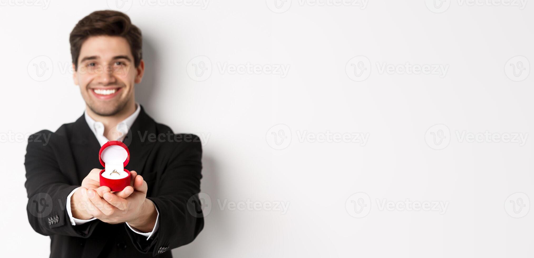 Image of handsome man looking romantic, giving you an engagement ring, making proposal to marry him, standing against white background photo