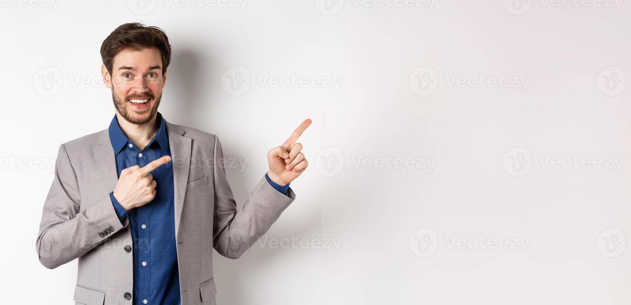Happy businessman in suit pointing fingers right and smiling excited, showing special deal, standing on white background photo