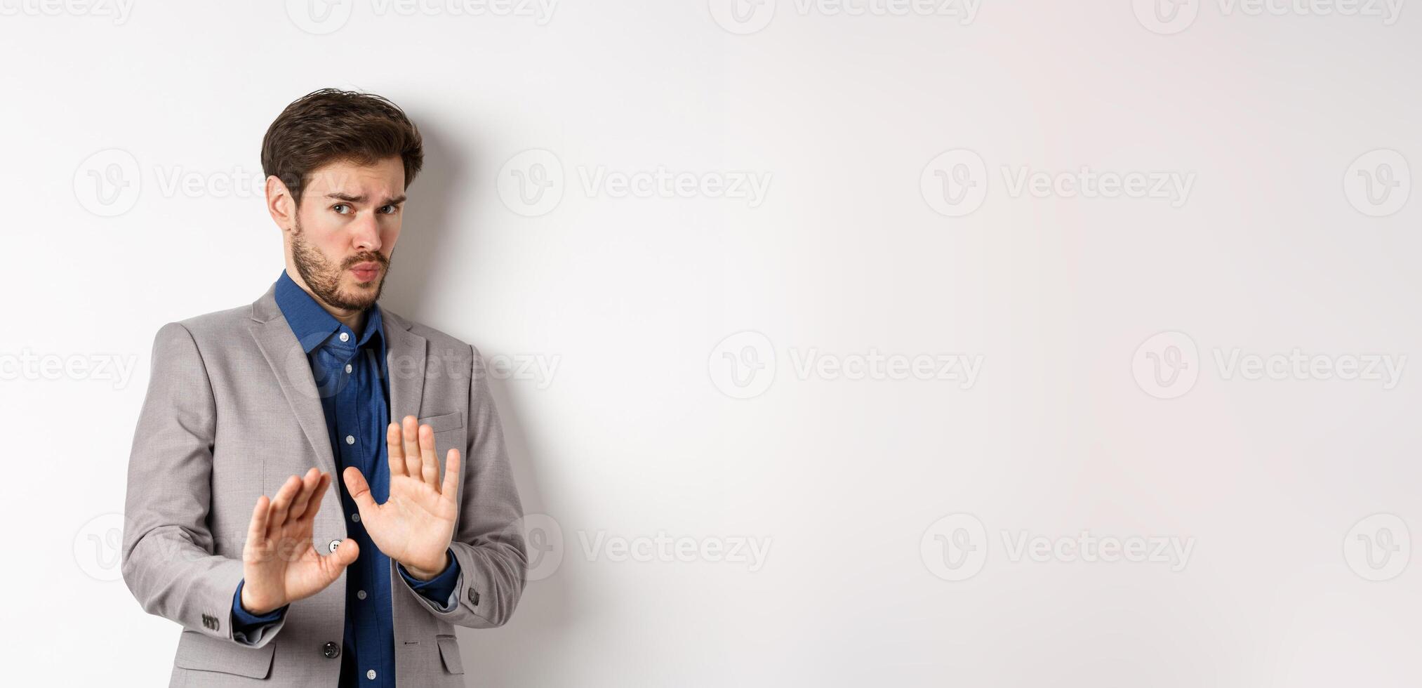 Stay away. Reluctant businessman step back with concerned disgusted face, raising hands to block bad offer, rejecting something awful, telling no and decline proposal, white background photo