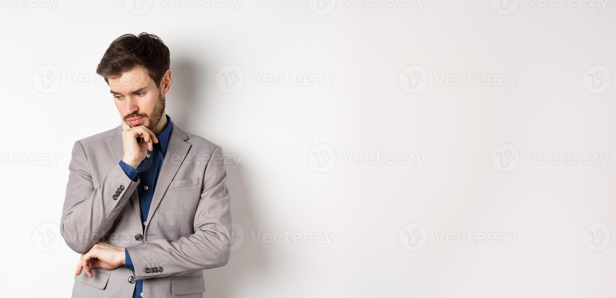 Thoughtful businessman in suit looking down and thinking, making decision, standing on white background photo