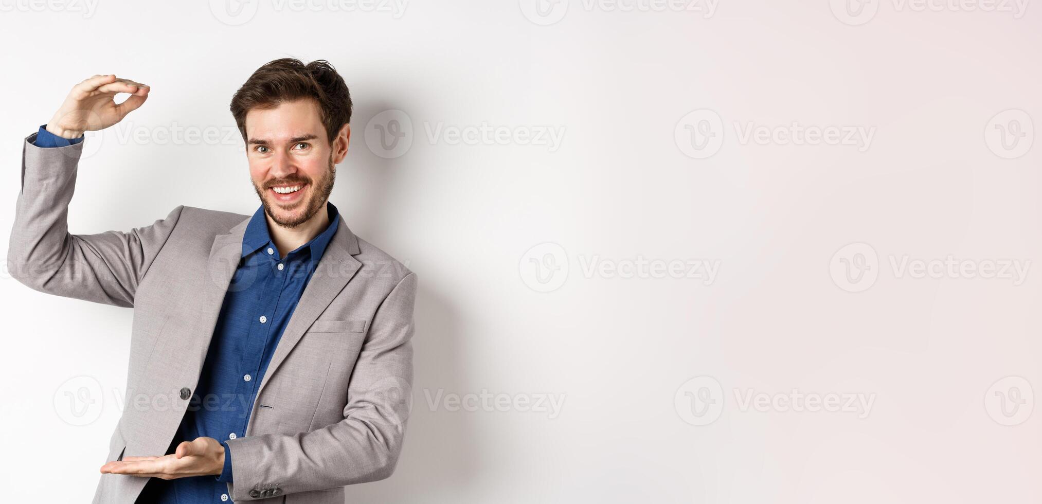 Successful businessman showing big size, shape large object and smiling pleased, standing on white background in suit photo