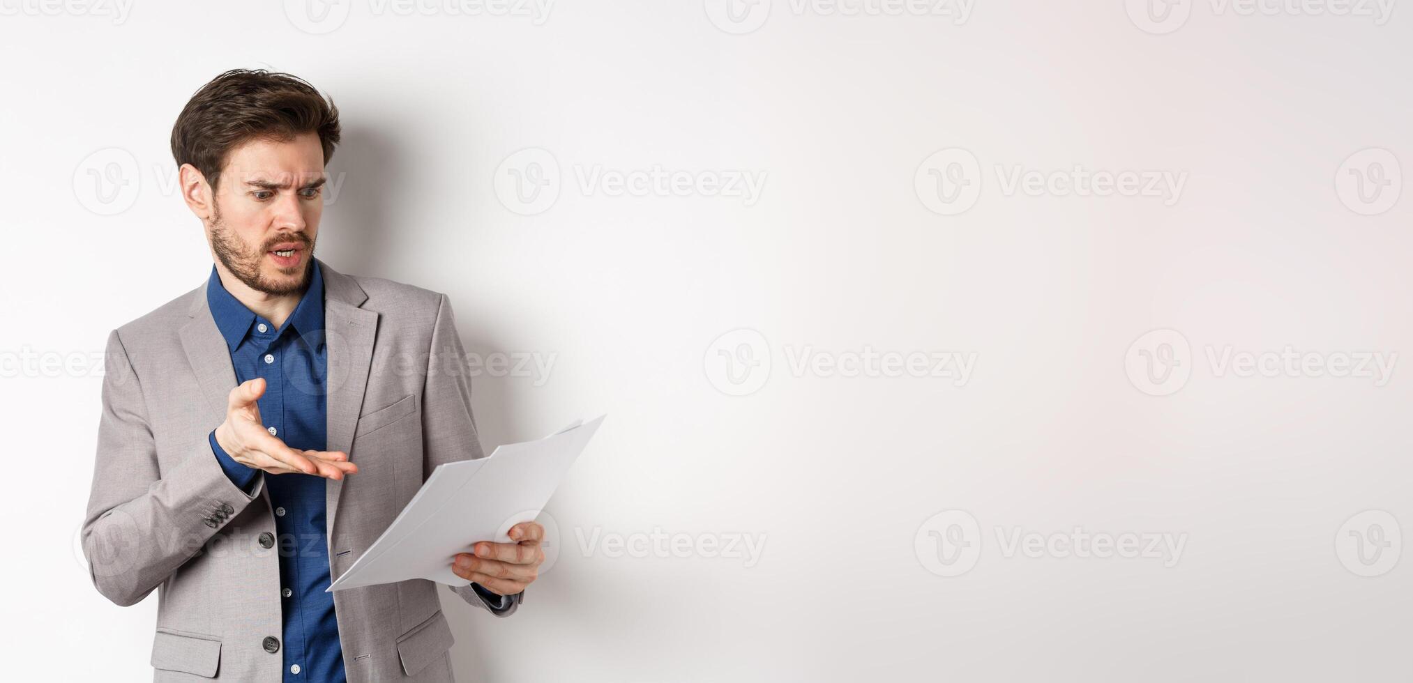 Angry employer looking at bad document, complaining on deal, pointing at paper frustrated, standing in suit on white background photo