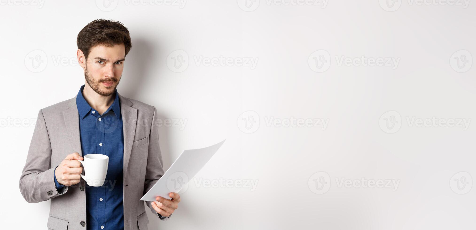 Businessman in suit reading documents papers and drinking coffee, smiling confident at camera, white background photo
