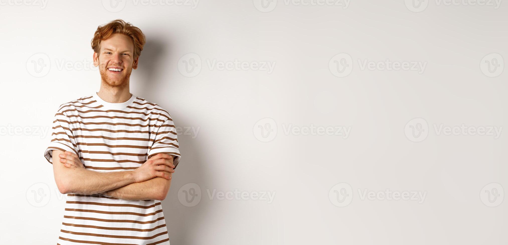 Happy redhead guy with bristle laughing and smiling at camera, standing with hands crossed on chest over white background photo