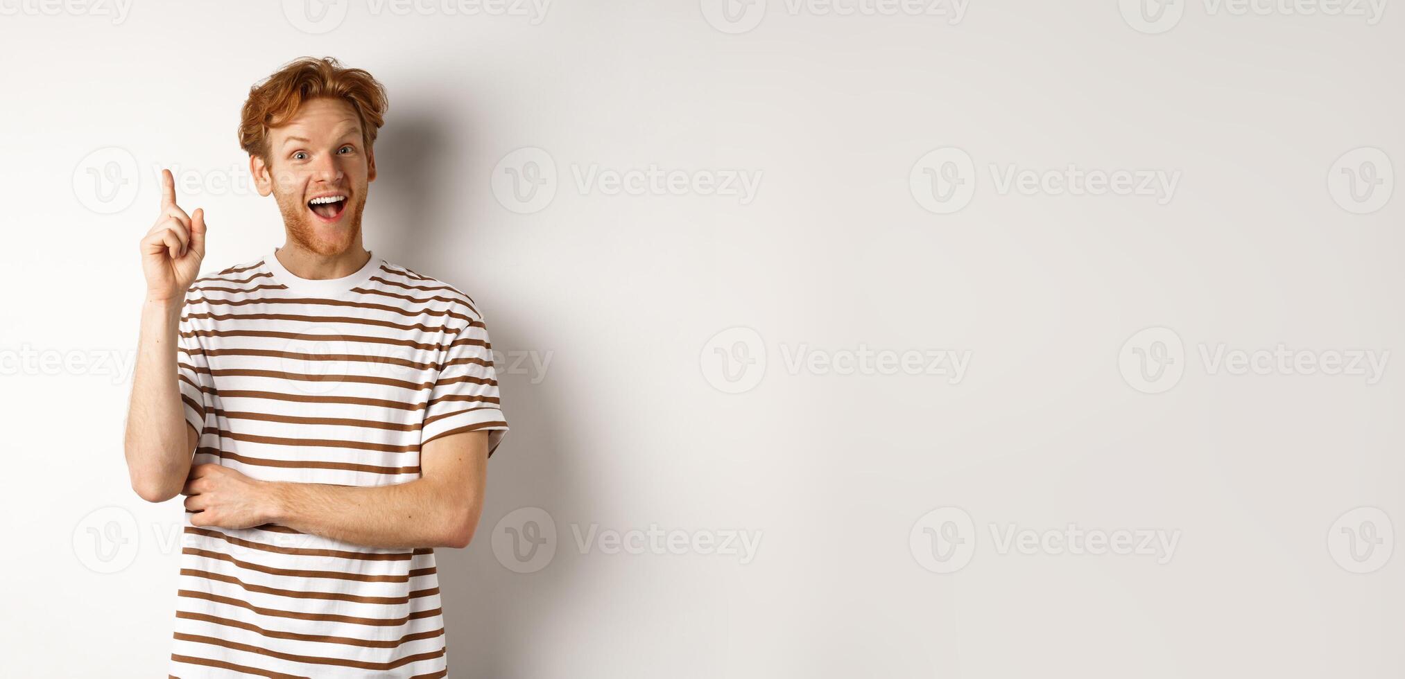 Young man with red hair having an idea, raising finger to say suggestion, standing happy over white background photo