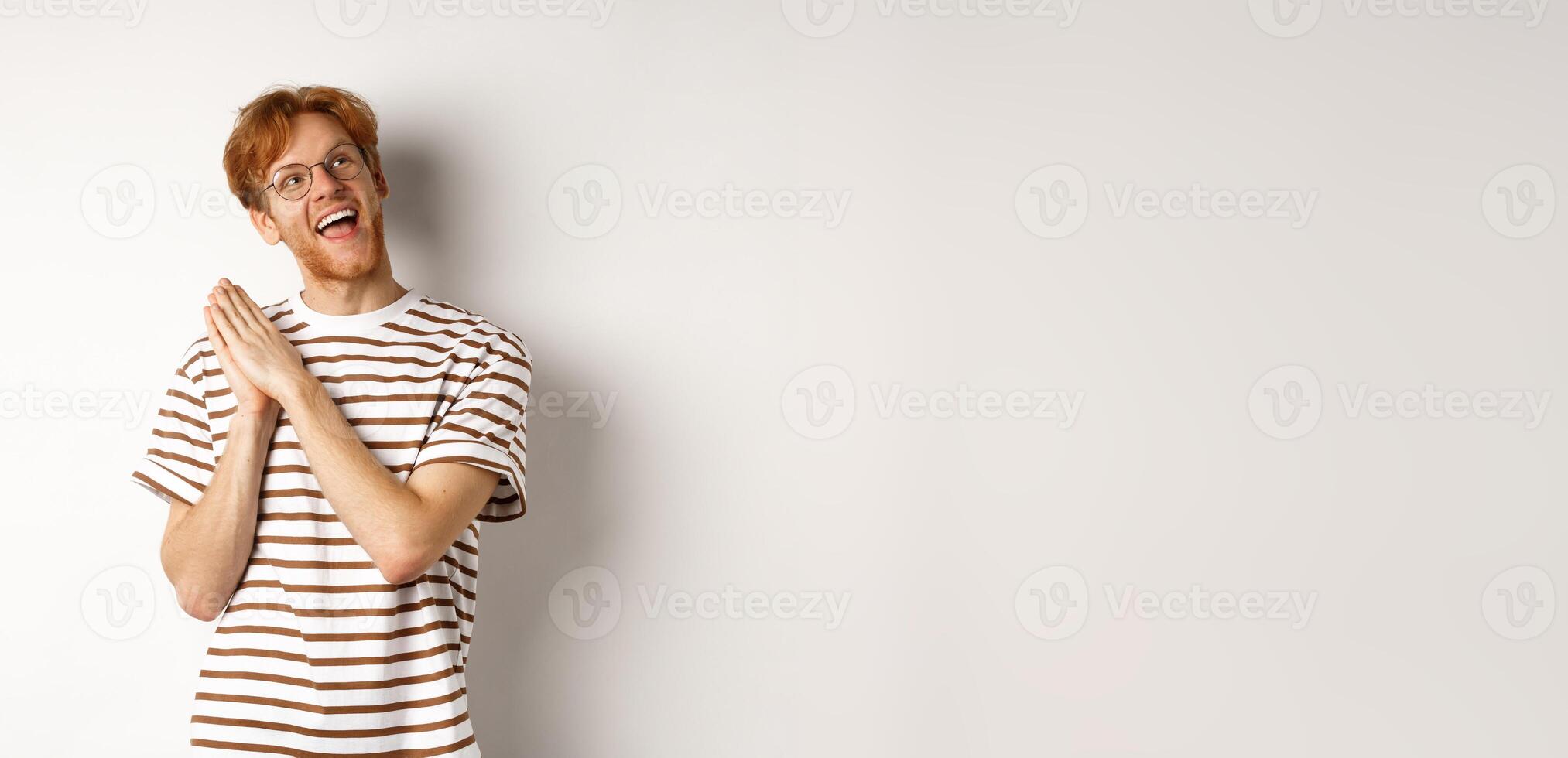Happy redhead man clap hands and looking satisfied at upper right corner, getting ready for something, standing over white background photo