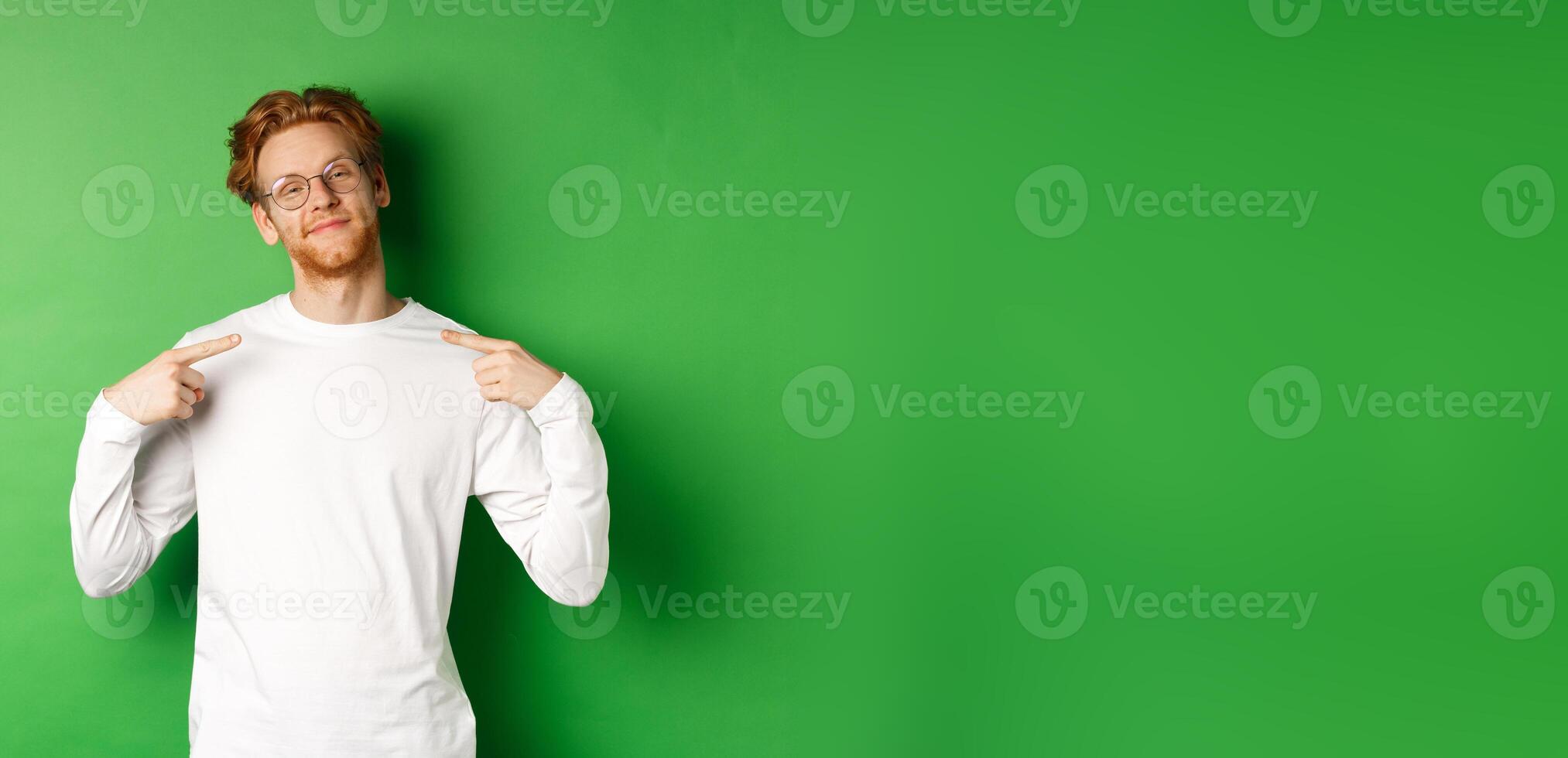 Confident and smug redhead man in glasses smiling, pointing at himself self-assured, standing over green background photo