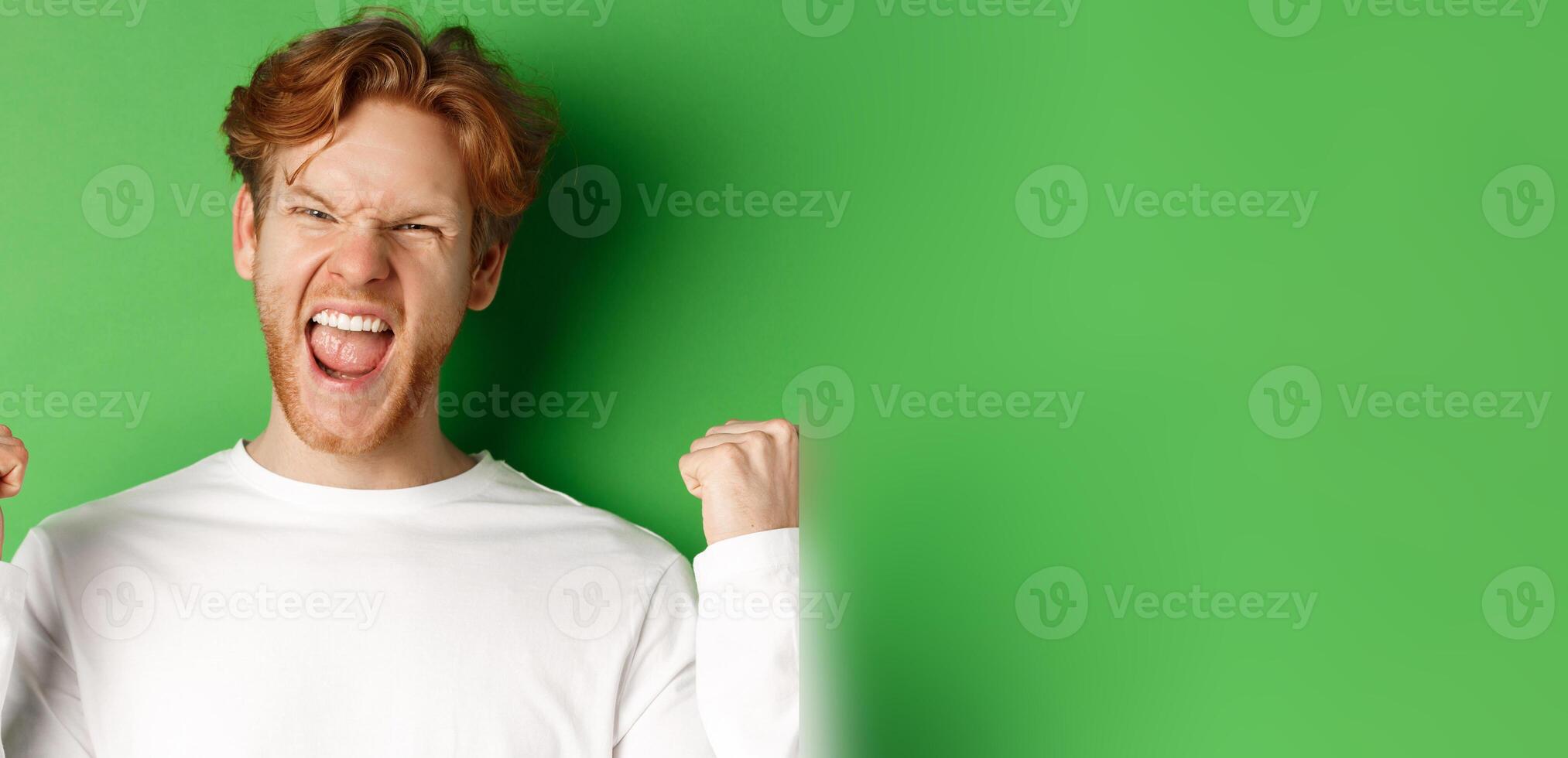 Close-up of lucky young man winner, celebrating victory, shouting yes with joy and making fist pumps, triumphing on green background photo