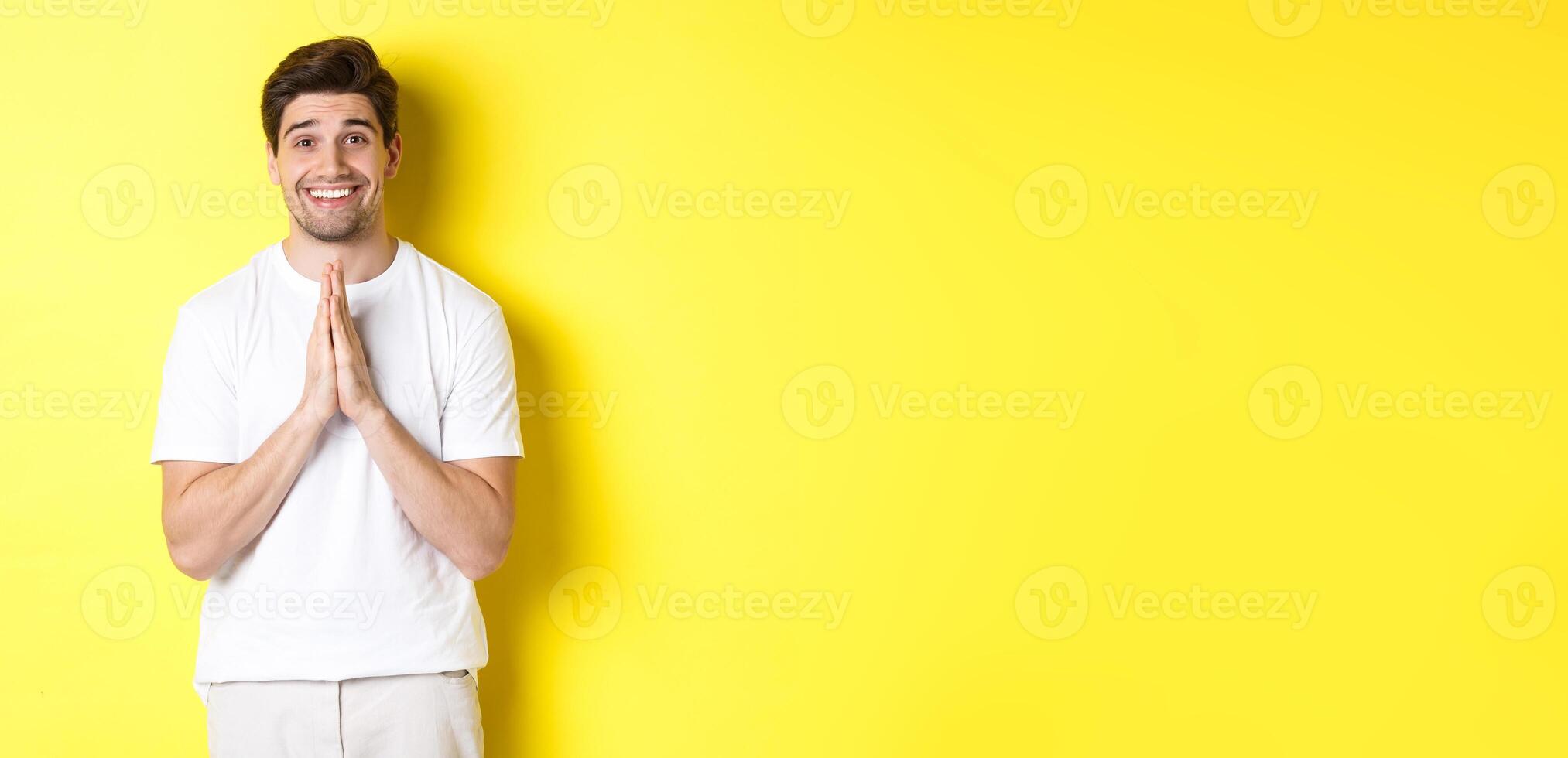 Hopeful man asking for help, begging favour, need something and smiling, standing over yellow background photo