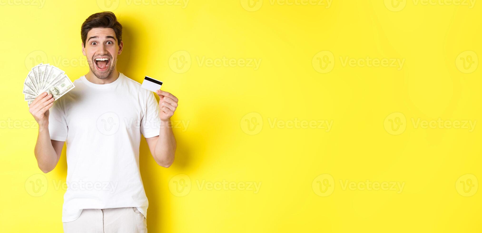 Excited man ready for black friday shopping, holding money and credit card, standing over yellow background photo