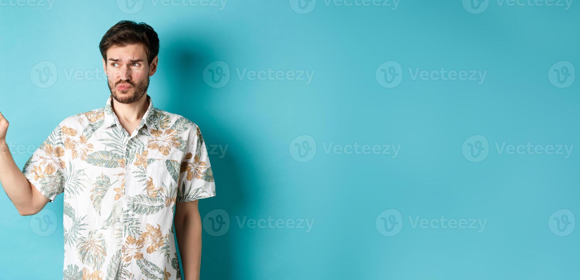 Displeased tourist in hawaiian shirt, looking and pointing left disappointed, complaining something bad, standing on blue background photo