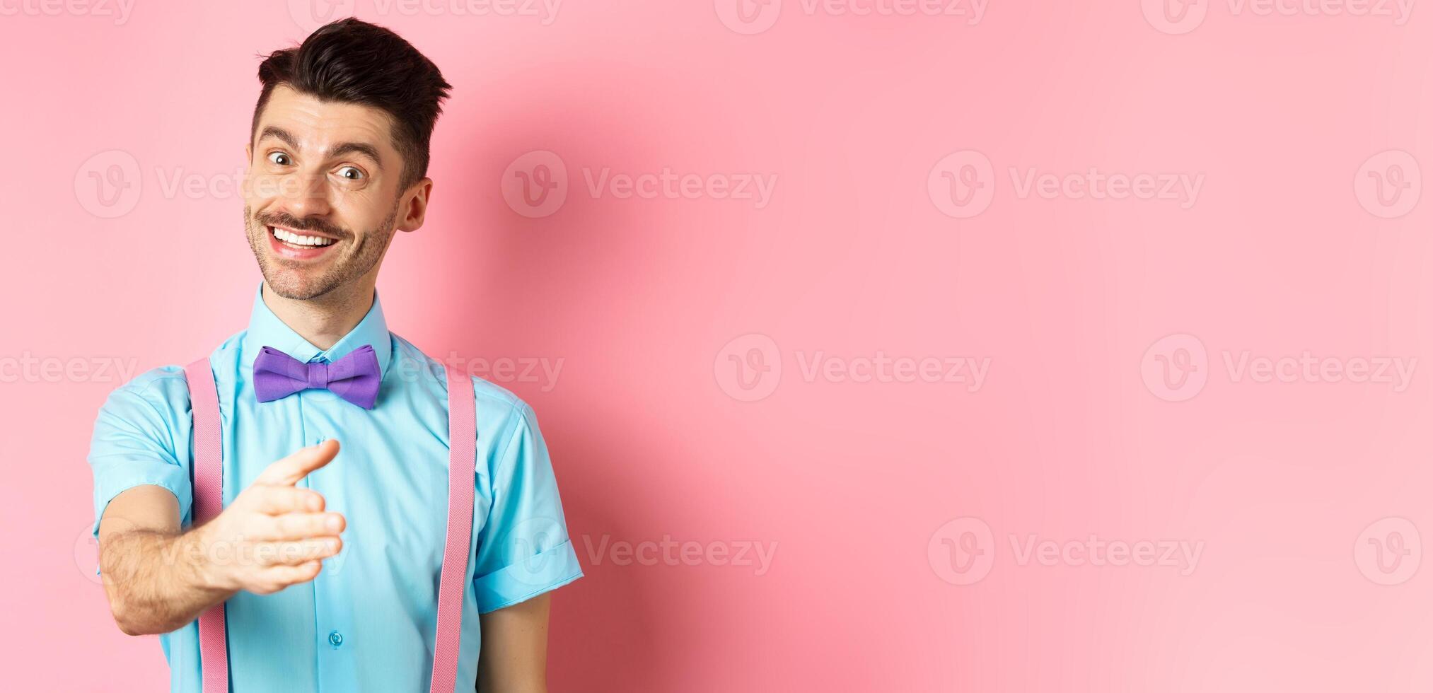 Nice to meet you. Handsome young man stretch out hand for handshake, smiling friendly and polite, introduce himself, standing over pink background photo