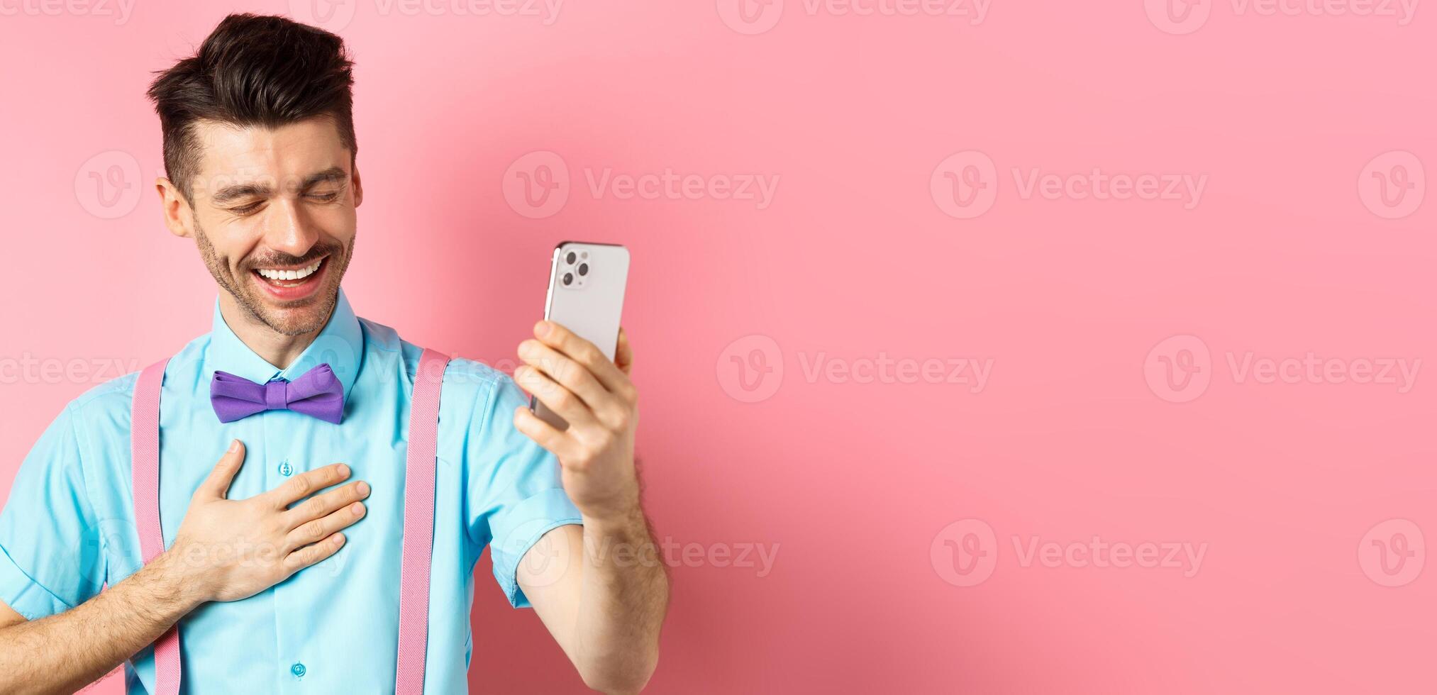 Image of handsome guy laughing during chat, having mobile conversation and chuckle from something funny, standing on pink background photo