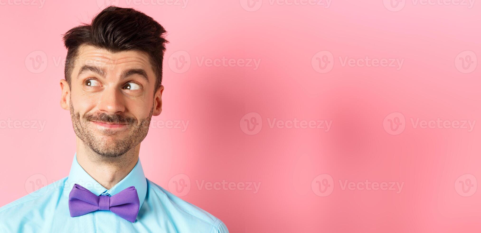 Close-up of handsome smiling guy with moustache, looking left at logo with pleased face, standing on pink background photo