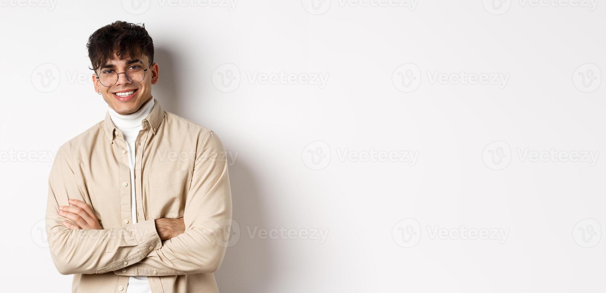 Handsome young man in glasses cross arms on chest, smiling at camera carefree, standing on white background photo