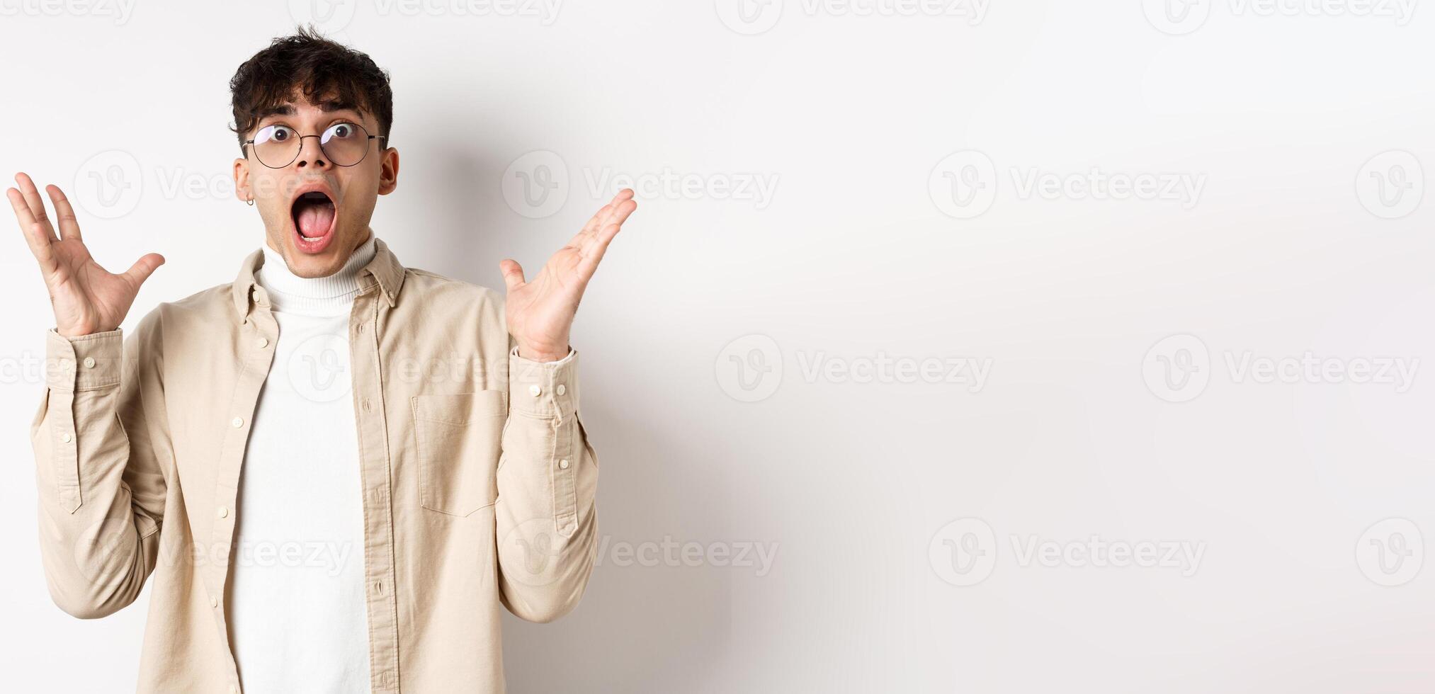 Scared young man in panic, screaming and looking axious, jumping startled and shocked, shaking hands nervously, standing on white background photo