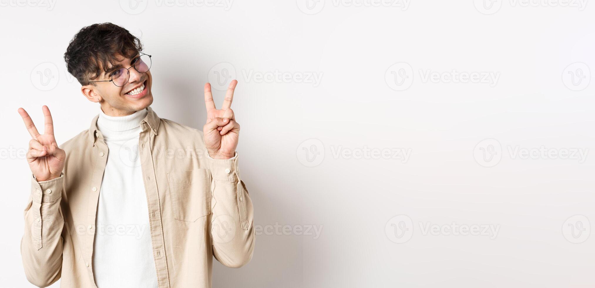 Real people. Handsome hipster guy in glasses showing peace gestures and smiling cute, standing on white background photo