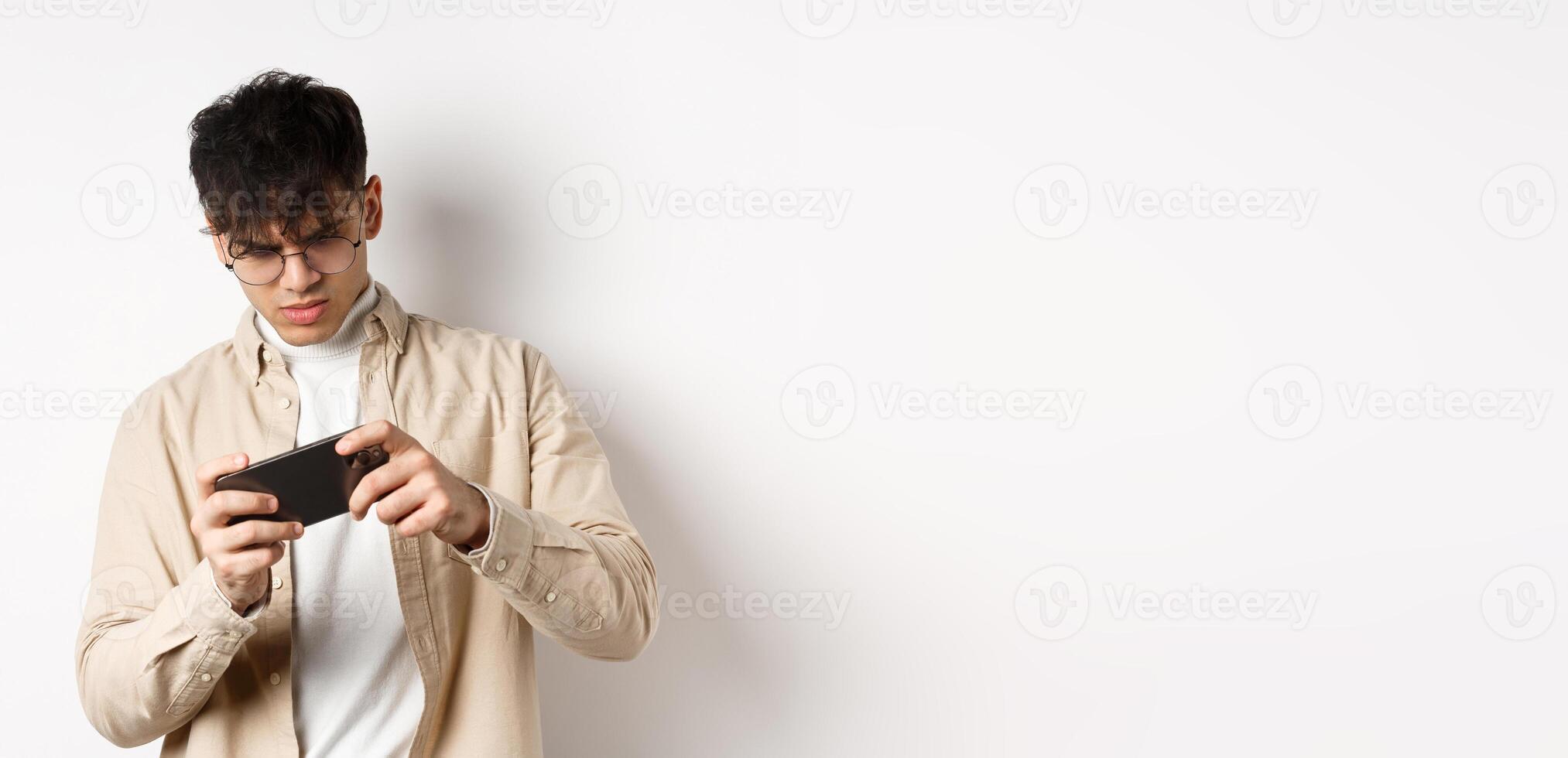 Portrait of handsome young man playing game on mobile phone, tilt smartphone to play racing, standing on white background photo