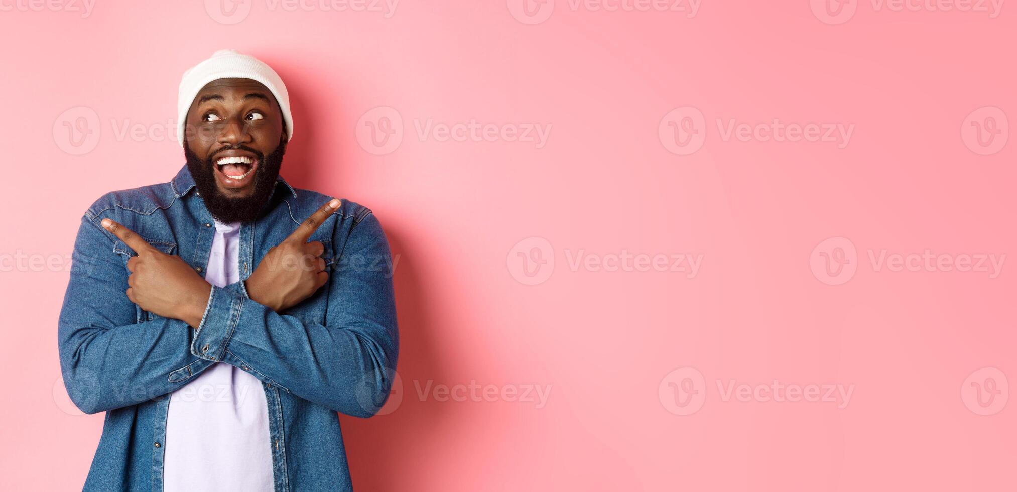 Excited young african-american man pointing sideways, showing two choices and making decision, smiling happy, standing over pink background photo