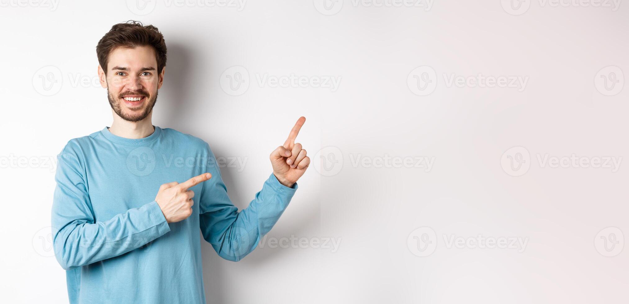 Happy bearded man showing advertisement, pointing fingers right and smiling, inviting to click link, standing over white background photo